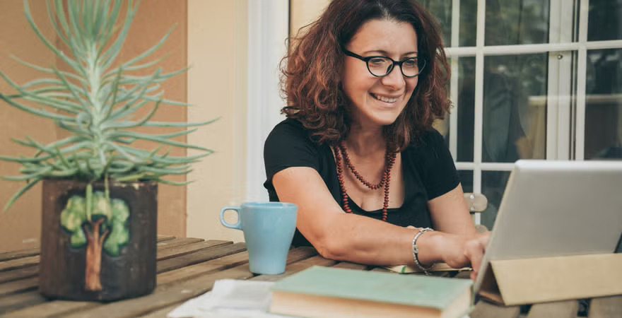 A woman studying at home, sitting at a table with an open laptop and notebook.