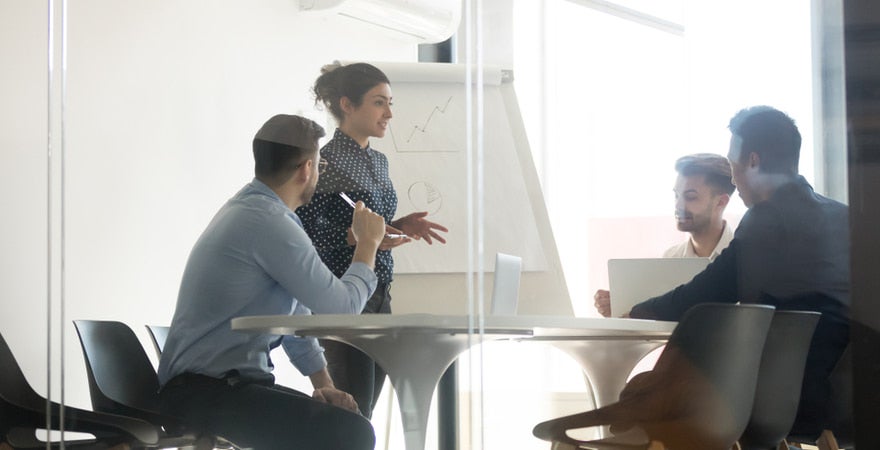 A counsellor stands in a room, talking to a team of corporate professionals.