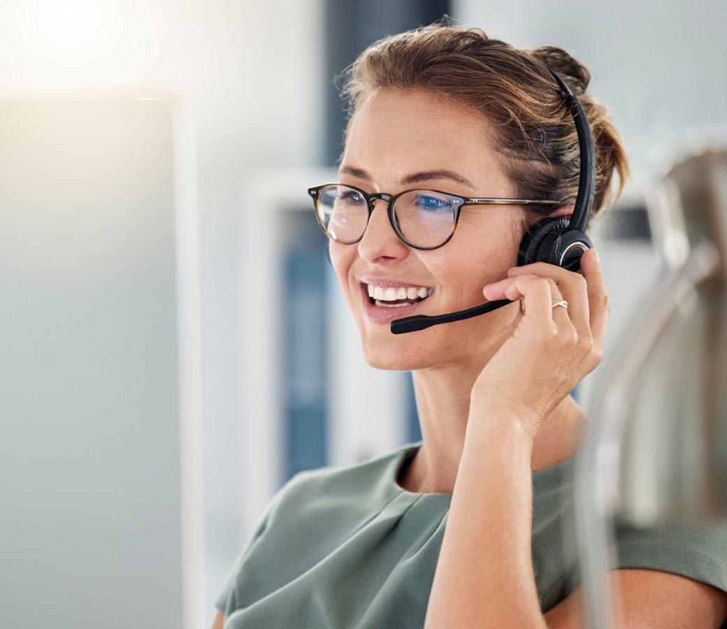 A woman with glasses and a headset is engaged in a phone conversation.