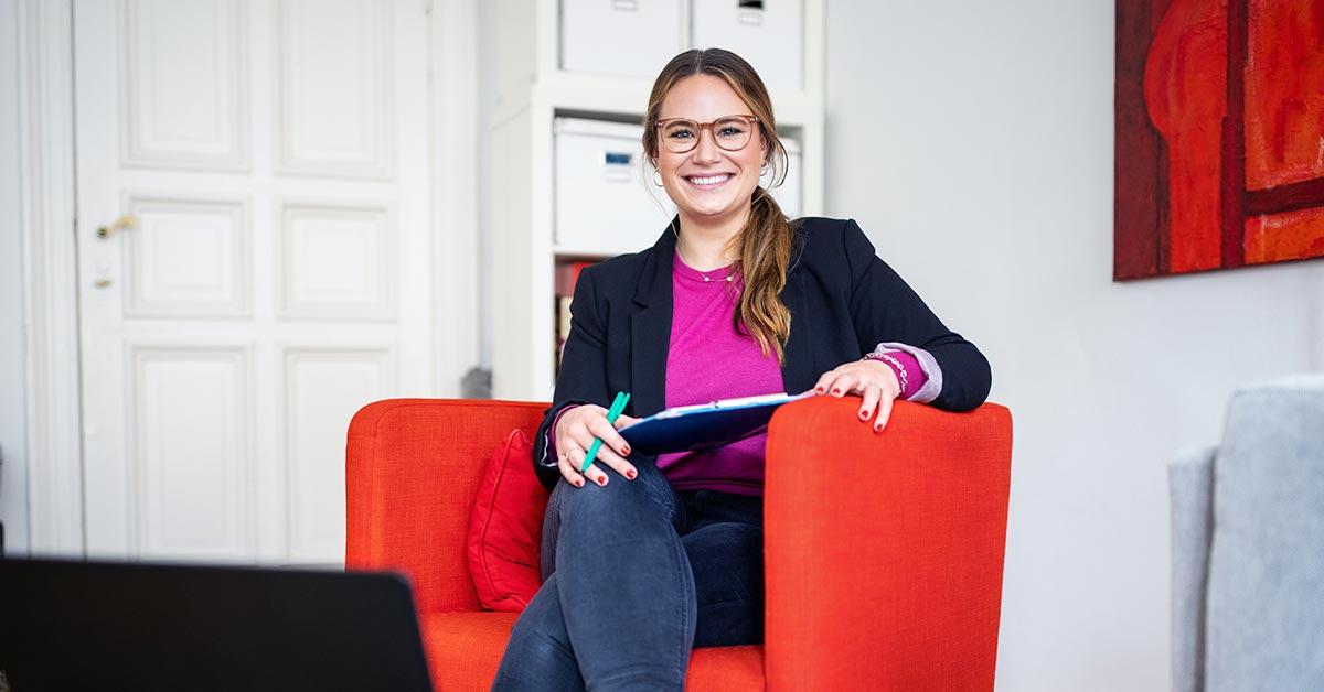 Woman sitting in orange chair using laptop.