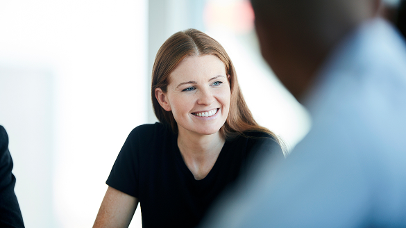 A smiling woman sits at a table with two other people, engaged in conversation and enjoying their time together.