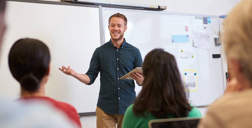 A senior male teacher presenting a motivational talk to a group of colleagues.