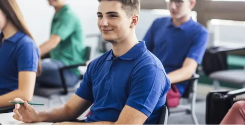 Young male student in blue polo shirt smiling confidently in classroom with diverse classmates in background