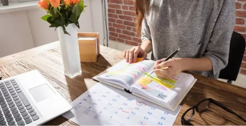 Student organizing planner and calendar at desk with laptop