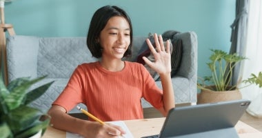 "Education student waving on video call with a pen in the other hand"